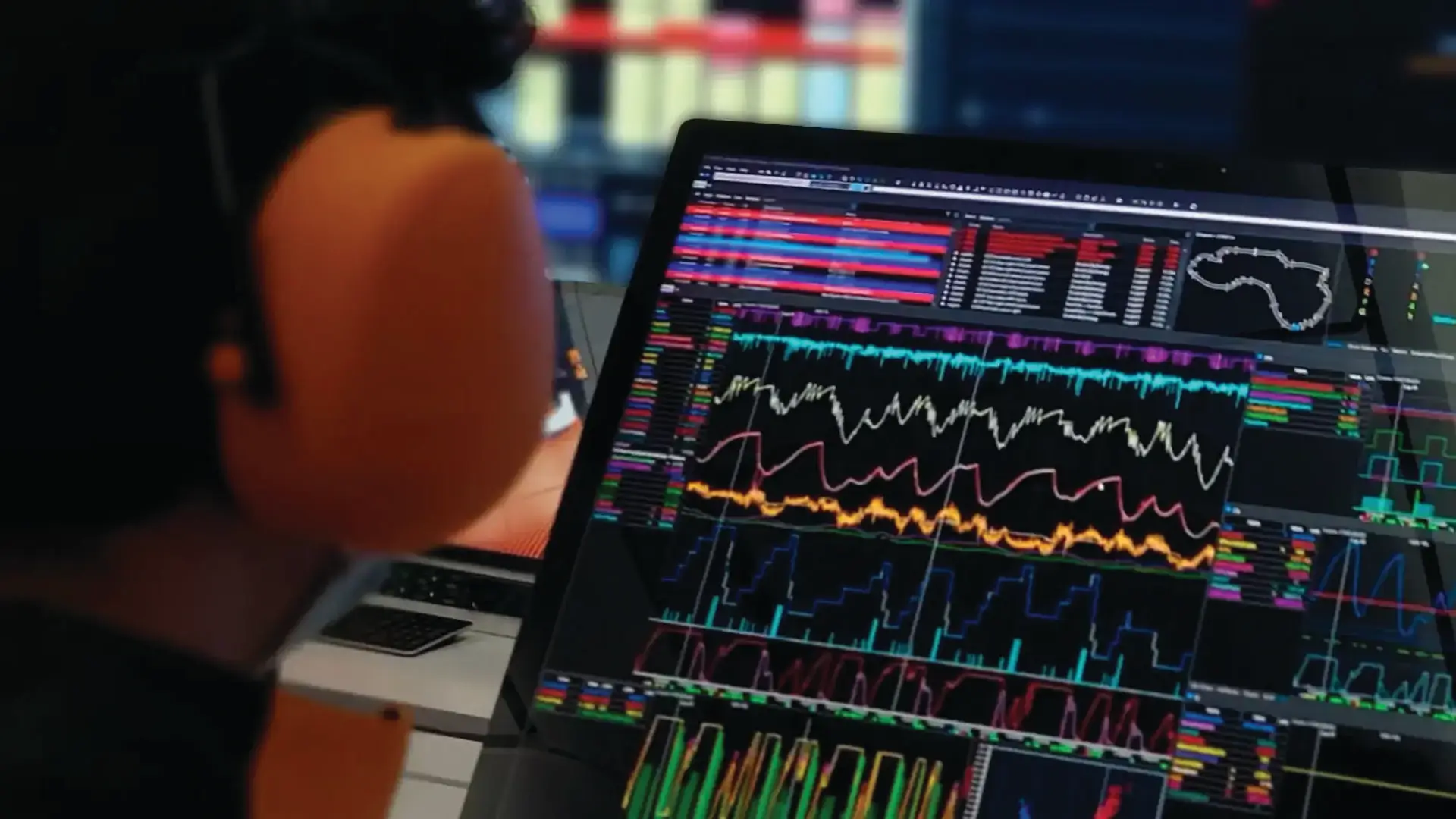 Person viewing a laptop displaying motorsport data analysis software with multiple telemetry graphs, performance charts, and a track map on screen.