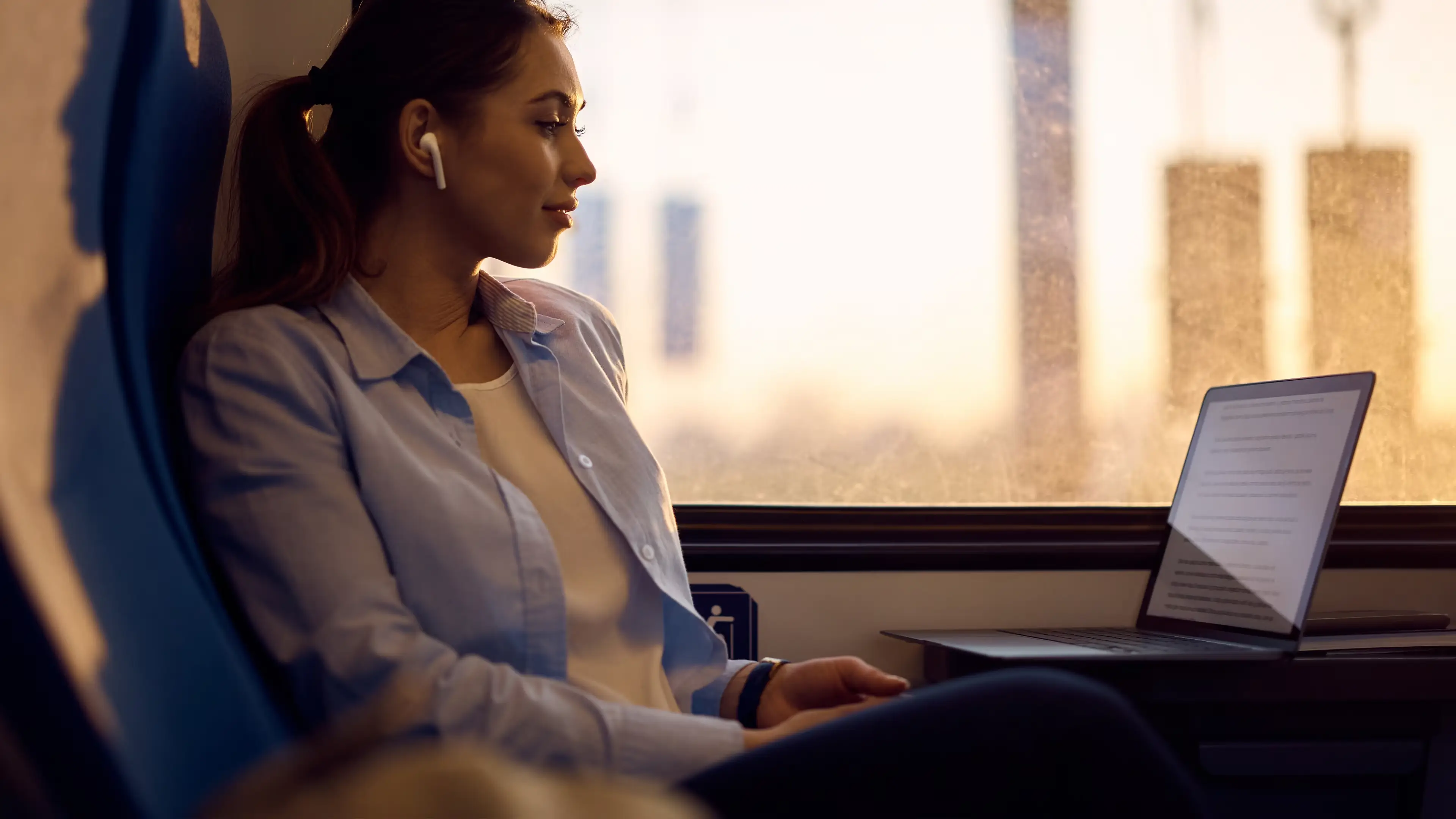 Woman sat on train with earphones in using her laptop